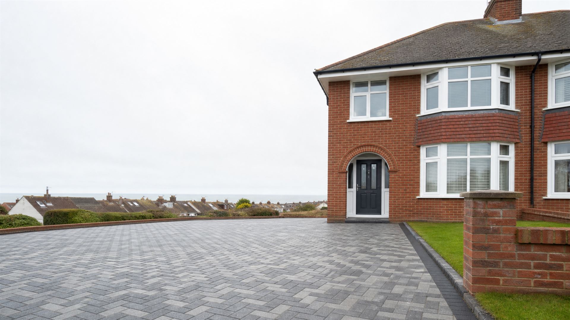 Red-brick house with a grey herringbone block-paved driveway